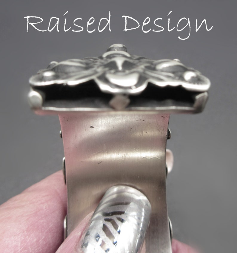 May include: A silver bracelet with a raised design of a butterfly. The bracelet is made of metal and has a polished finish.