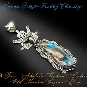 May include: A silver pendant with a turquoise stone and intricate designs. The pendant is a three-tiered "Shalako Kachina" pendant with a Pilot Mountain turquoise drop. The artist is Freddy Charley.