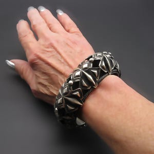 May include: A silver bracelet with a geometric design. The bracelet is made of multiple pieces that are connected together to form a circle. The bracelet is worn on a person's wrist.