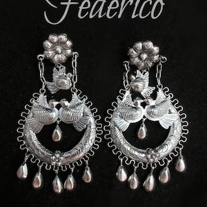 May include: A pair of silver earrings with a floral design and two doves. The earrings are made of sterling silver and have a dangling design with multiple drops.