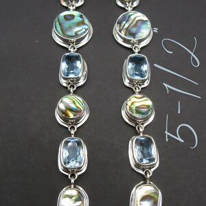 May include: A pair of silver dangle earrings with blue and iridescent abalone shell accents. The earrings are 5 1/2 inches long.