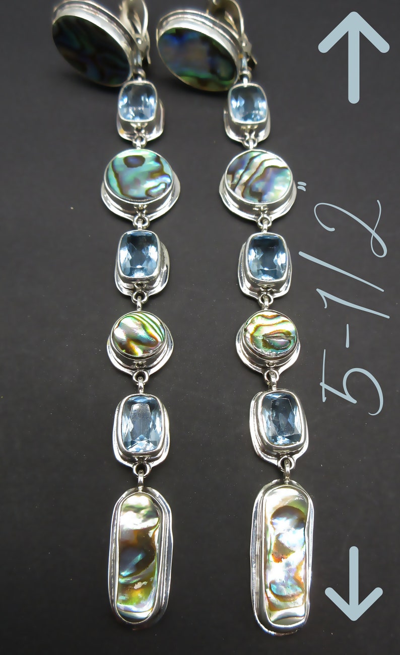 May include: A pair of silver dangle earrings with blue and iridescent abalone shell accents. The earrings are 5 1/2 inches long.