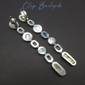 May include: A pair of silver clip-on earrings with a long, dangling design. Each earring features a series of oval-shaped, iridescent abalone shell stones separated by small, black square stones. The earrings are marked with the text "T.H. Designs".