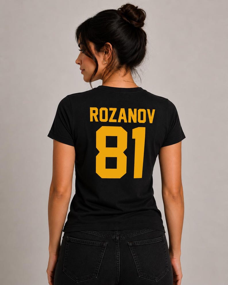 May include: Black t-shirt with the name "ROZANOV" and the number "81" printed in gold. The shirt is made of a soft material and is visible from the back. The model is wearing black jeans.
