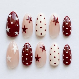 May include: A set of ten almond-shaped press-on nails featuring a mix of designs. Some nails are deep burgundy with white polka dots or white stars, while others are cream with burgundy dots or stars, and some are clear with burgundy or white stars.