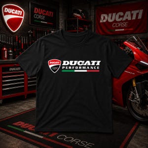 May include: A black short-sleeved t-shirt featuring the white text DUCATI PERFORMANCE, the Ducati Corse shield logo, and a horizontal stripe in green, white, and red colours printed across the centre of the chest area on the front of the garment.