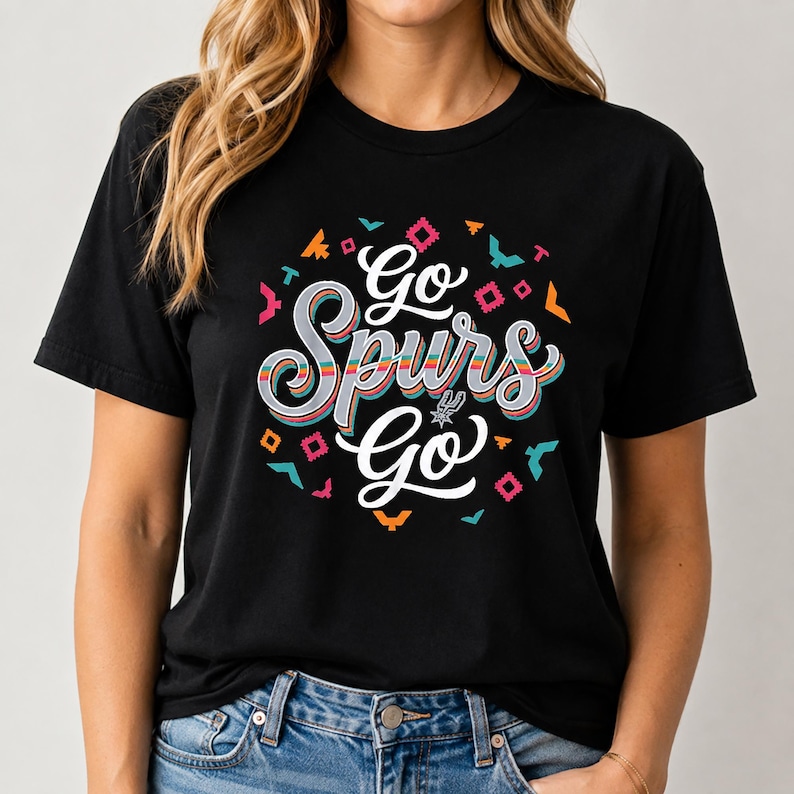 May include: Black t-shirt featuring the text "Go Spurs Go" in a colourful, stylised font. The design incorporates geometric shapes in orange, pink, teal, and yellow. The shirt has a classic crew neck.