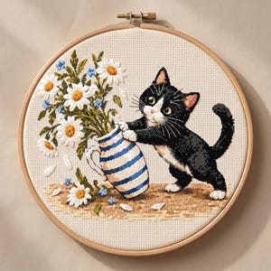 Può includere: Un ricamo a punto croce in un telaio di legno rotondo raffigurante un gatto bianco e nero in piedi sulle zampe posteriori, che spinge una brocca in ceramica a righe blu e bianche piena di margherite bianche e piccoli fiori blu su una base.