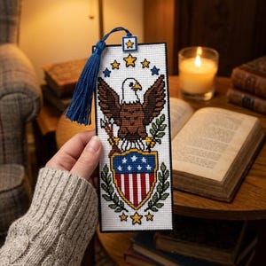 Peut inclure: Un marque-page en point de croix sur toile Aida blanche représentant un pygargue à tête blanche avec des ailes brunes, une tête blanche et un bec jaune. Sous l'aigle se trouve un écusson aux rayures rouges et blanches et étoiles bleues.