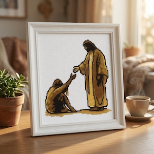 Può includere: Un ricamo a punto croce incorniciato che presenta un design pixelato di una figura in piedi con una lunga veste dorata, che tende la mano verso una figura più piccola seduta. L'opera è esposta in una cornice quadrata in legno bianco.