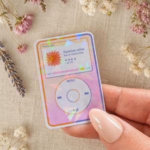 May include: A rectangular holographic sticker featuring a digital music player interface. The screen displays the text 'Now playing', 'Summer mine', 'Sun ft. Good vibes', and a four-star rating. Below, a circular control pad includes 'MENU' and playback icons.