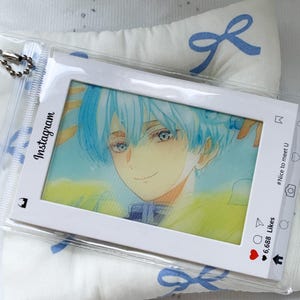 May include: A clear plastic card holder featuring a white frame designed like an Instagram post. The insert displays an anime-style illustration of a person with light blue hair and a yellow garment. The frame includes icons and the text #Nice to meet U.