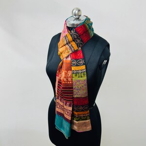 May include: A rectangular scarf featuring a patchwork design of various colorful fabric panels. The scarf displays a mix of red, orange, yellow, green, and teal hues with diverse printed patterns including leaf motifs, stripes, and geometric shapes.