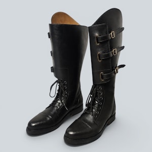 May include: A pair of black leather riding boots. The boots have a lace-up design at the foot and three buckle straps on the upper shaft. The boots are knee-high and have a pointed toe.