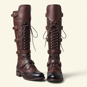 May include: A pair of knee-high brown leather boots featuring a textured finish, front lace-up closures with metal eyelets, and four adjustable buckled straps along the shaft. The boots have a dark, burnished toe cap with subtle brogue detailing.
