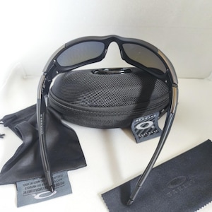 May include: Black sunglasses with a black case, cleaning cloth, and drawstring bag. The sunglasses have a curved frame and dark lenses. The case is textured and has a zipper. The drawstring bag and cleaning cloth are black.
