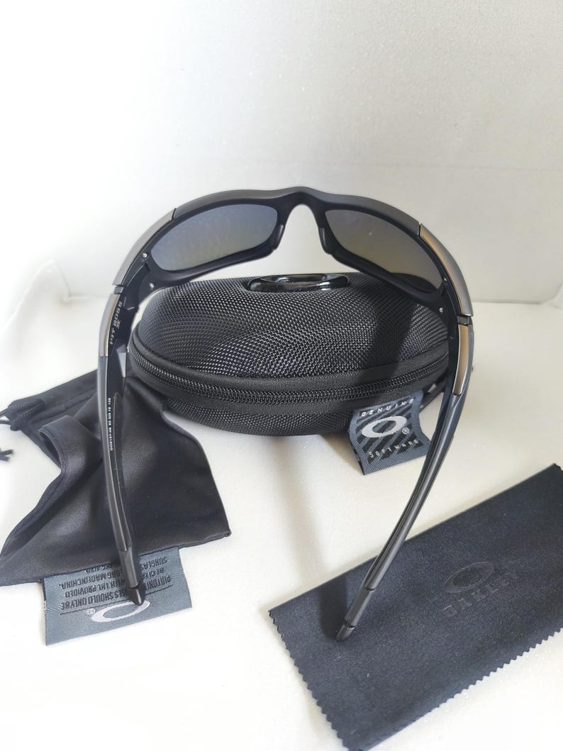 May include: Black sunglasses with a black case, cleaning cloth, and drawstring bag. The sunglasses have a curved frame and dark lenses. The case is textured and has a zipper. The drawstring bag and cleaning cloth are black.