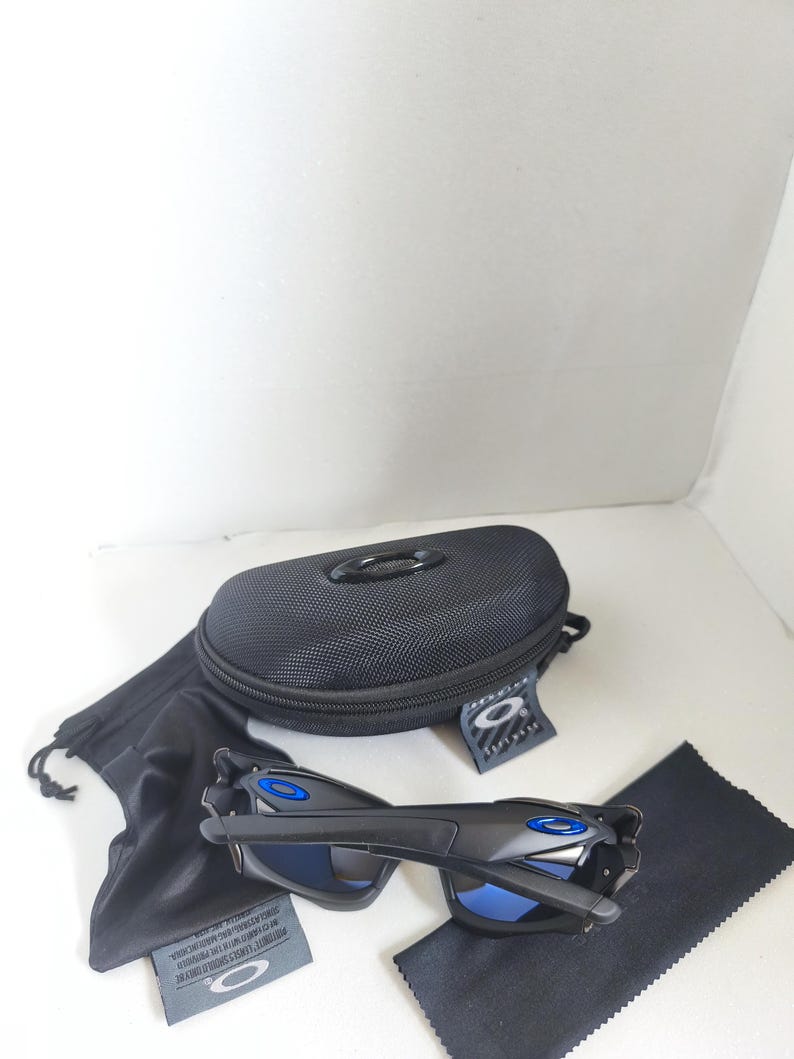May include: Black sunglasses with blue lenses and accents, a black case, a black drawstring bag, a black cleaning cloth, and a tag. The sunglasses have a sleek, modern design. The case has a zipper closure and the brand logo.