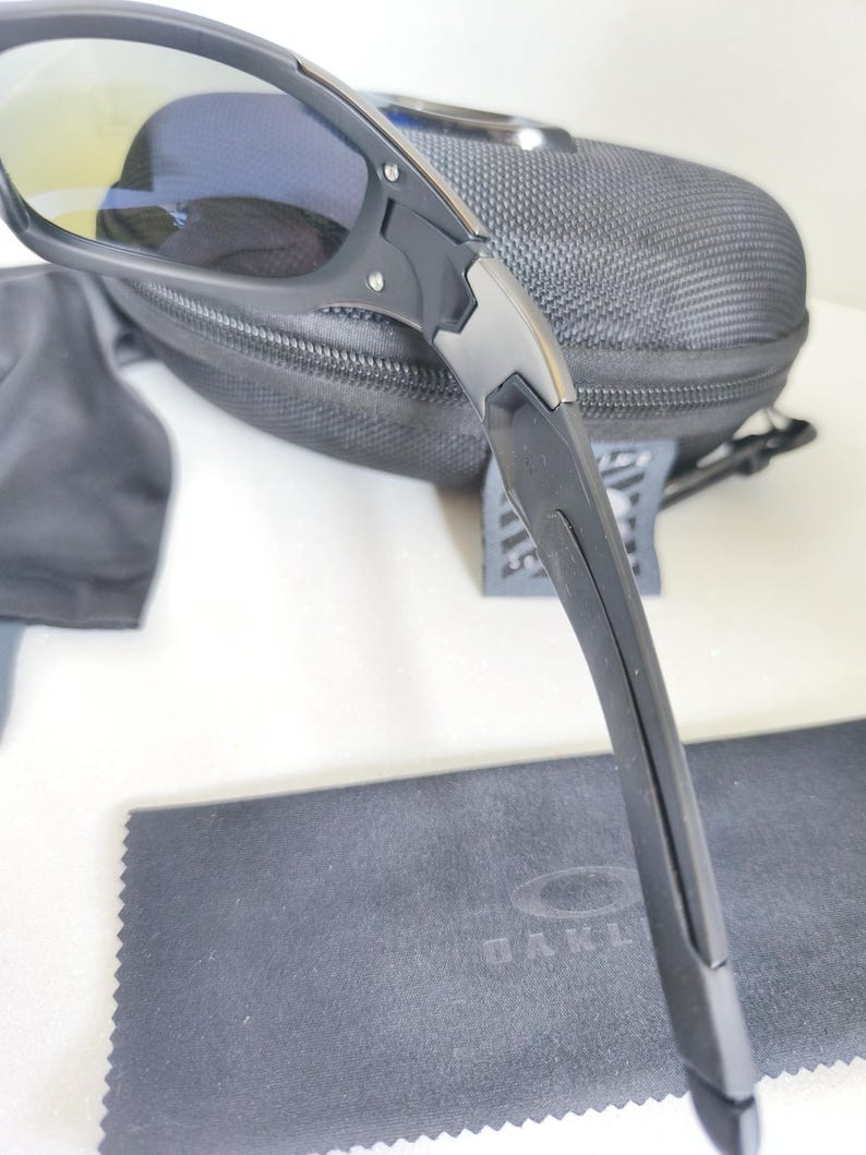 May include: Black sunglasses with a black case and cleaning cloth. The sunglasses have a sleek, modern design with a black frame and tinted lenses. The case is a dark gray, zippered, and the cleaning cloth has the brand name printed on it.