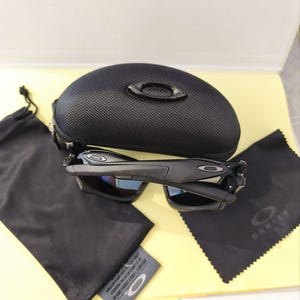 Puede incluir: Gafas de sol negras con estuche a juego, pa&ntilde;o de microfibra y bolsa con cord&oacute;n. Las gafas tienen un dise&ntilde;o elegante con lentes oscuras y montura negra. El estuche es texturizado y tiene un peque&ntilde;o logotipo.