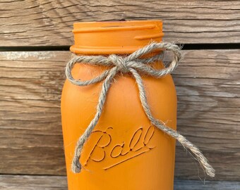 May include: Orange glass mason jar with a brown twine bow. The jar has the words "Ball" and "Mason" embossed on the front.
