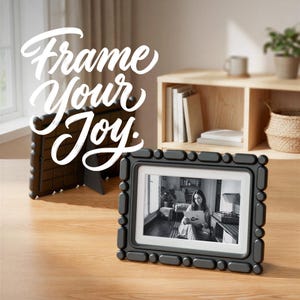 Può includere: Una cornice digitale nera con un bordo testurizzato a forma di pillola. Lo schermo mostra una fotografia in bianco e nero di una persona che tiene in mano un disco. Il testo "Frame Your Joy" è sovrapposto in bianco in alto a sinistra.