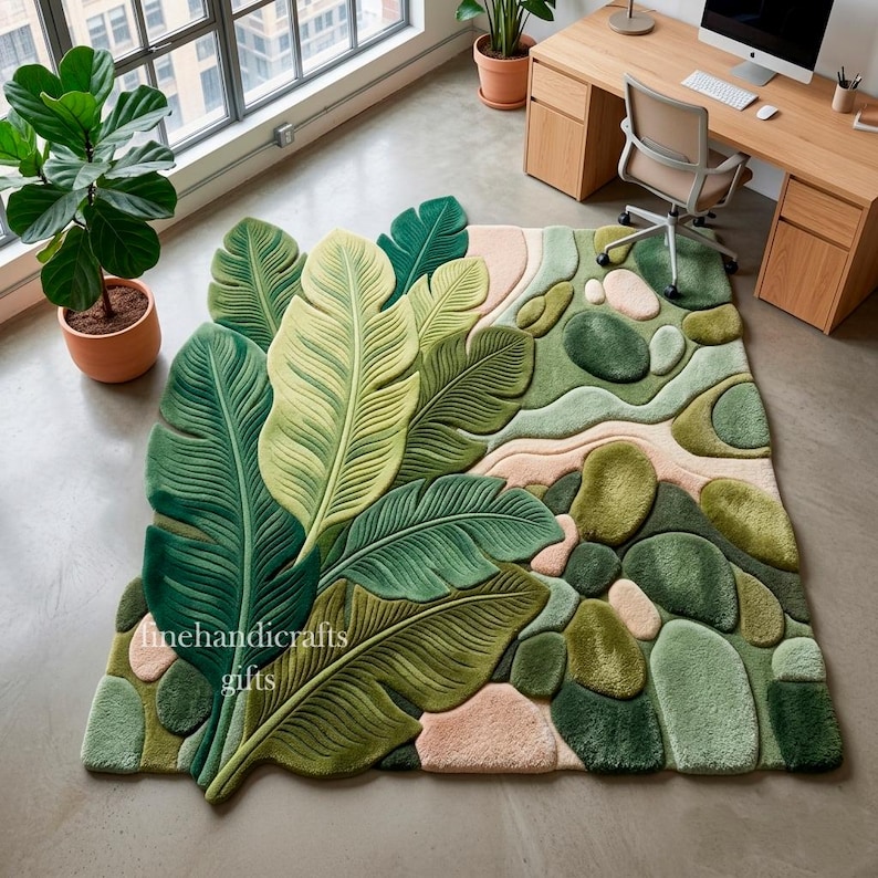 Puede incluir: Una alfombra de pelo insertado con un dise&ntilde;o a gran escala de hojas tropicales superpuestas en tonos verde oscuro y claro, contrastado por una secci&oacute;n de formas redondeadas similares a guijarros en verde suave y rosa p&aacute;lido, con el texto finehandicrafts gifts.