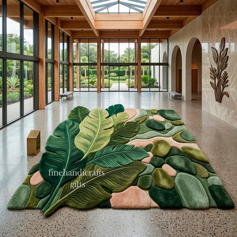 Puede incluir: Una alfombra rectangular con un dise&ntilde;o texturizado en tres dimensiones de grandes hojas tropicales superpuestas en tonos verde oscuro y claro, intercaladas con formas redondeadas y suaves similares a guijarros en verde y rosa suave. Texto finehandicrafts gifts.