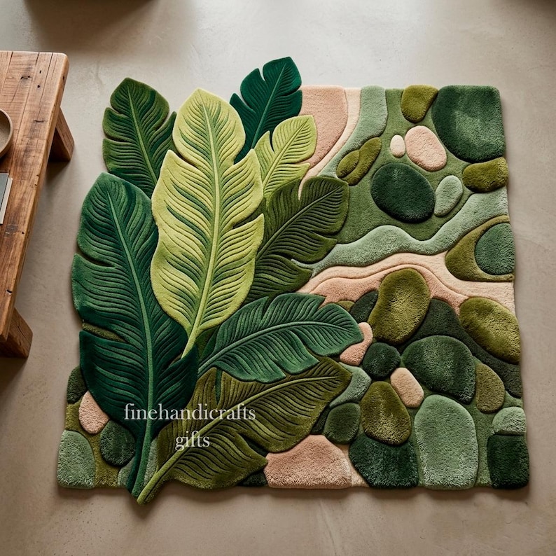 Puede incluir: Una alfombra rectangular con un dise&ntilde;o de mechones de grandes hojas tropicales superpuestas en tonos verde oscuro y claro, junto a un patr&oacute;n de formas de guijarros suaves y redondeados en tonos verdes y beige suave, con el texto finehandicrafts gifts.