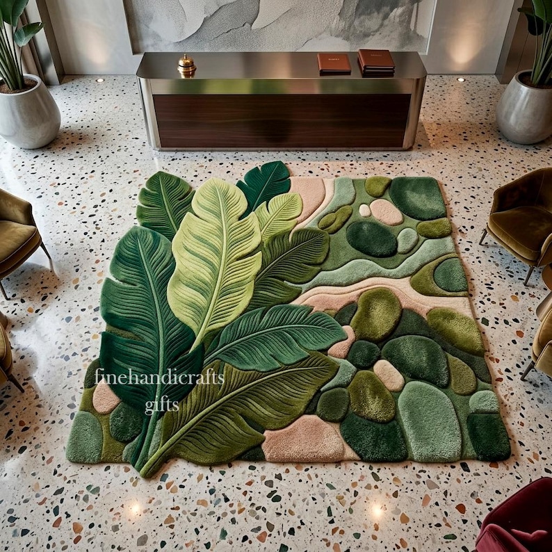 Puede incluir: Una alfombra rectangular que presenta un dise&ntilde;o a gran escala de hojas tropicales verdes superpuestas en un lado y un patr&oacute;n de formas redondeadas similares a guijarros en tonos verdes y beige en el otro. El texto finehandicrafts gifts es visible.