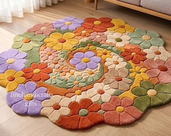 Puede incluir: Una alfombra redonda con mechones que presenta un patrón en espiral de flores multicolores en tonos naranja, amarillo, lavanda, verde salvia y crema. El texto "finehandicrafts gifts" está impreso en blanco en el lado izquierdo de la alfombra.