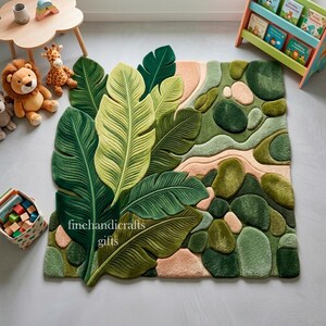 Puede incluir: Una alfombra de pelo insertado con un gran dise&ntilde;o bot&aacute;nico que presenta hojas de palmera verdes superpuestas en un lado y un patr&oacute;n texturizado de formas redondeadas similares a guijarros en tonos verdes y melocot&oacute;n suave. El texto finehandicrafts gifts es visible.