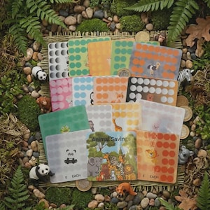 May include: A collection of square Animal Savings challenge cards featuring various colours and animal illustrations, including a panda, giraffe, and elephant. Each card has a grid of circles for tracking savings, with some cards labelled £ EACH.