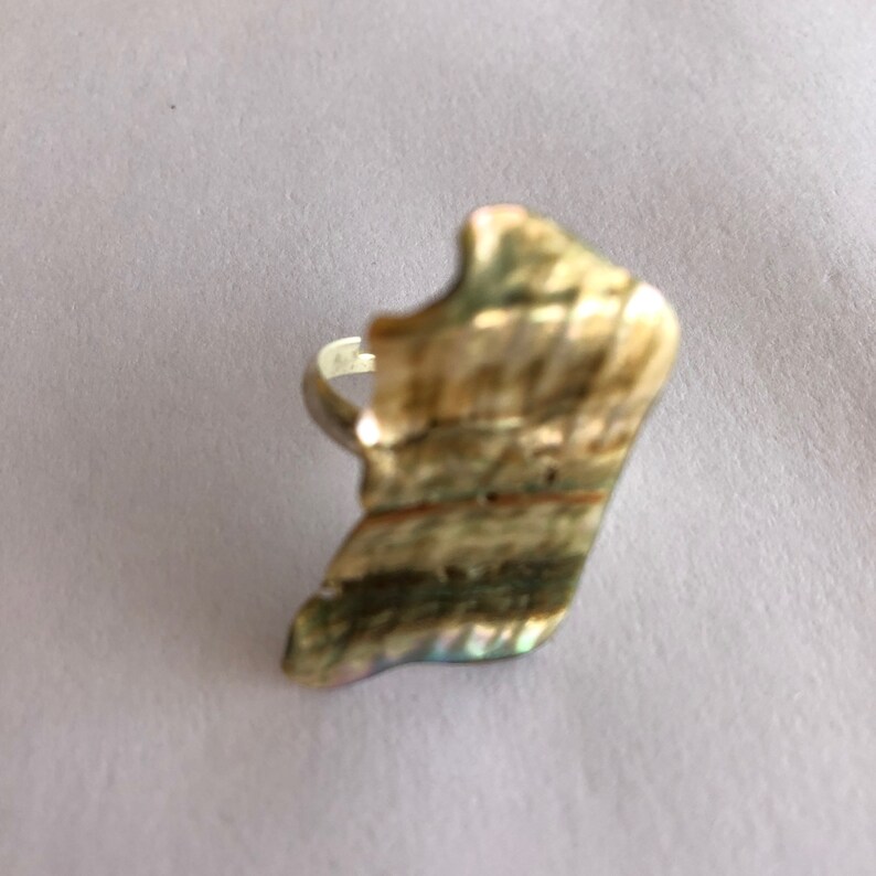 May include: A silver ring with a large, iridescent, irregular-shaped shell as the face.