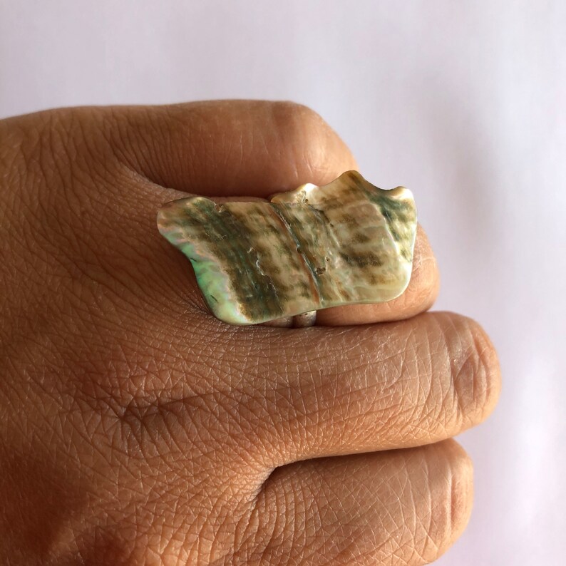 May include: A large, iridescent green and brown shell ring. The ring is made from a natural shell and has a unique, organic shape.