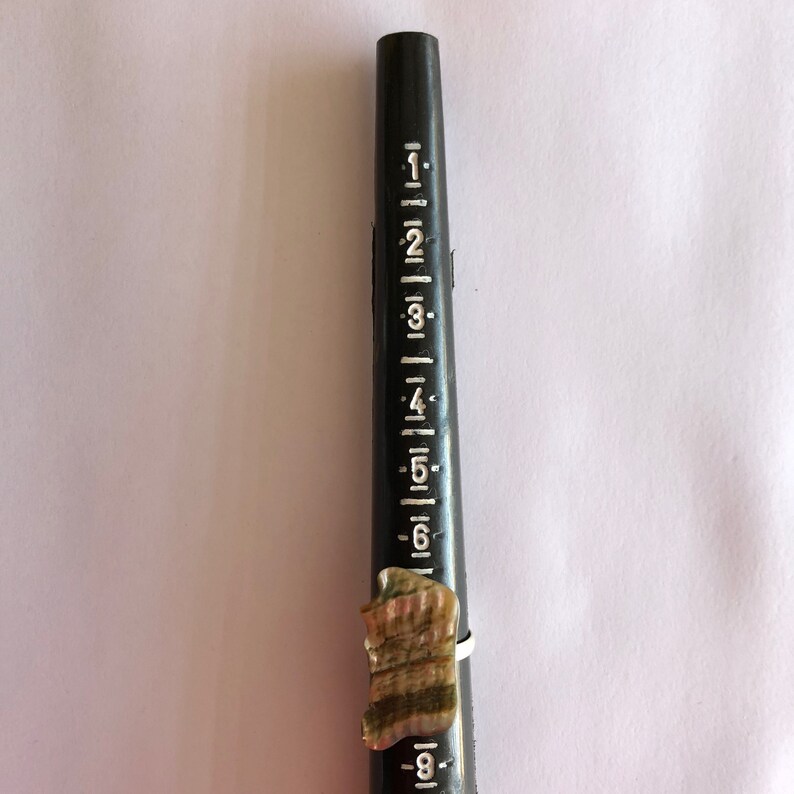May include: A ring sizer with a ring on it. The ring is made of a brown and white shell material. The ring sizer is black and has white markings from 1 to 8.