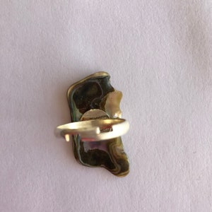 May include: A silver ring with a large, irregularly shaped, iridescent abalone shell set in the centre.