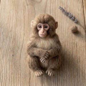 May include: A needle-felted monkey figurine with textured brown and tan fur, dark eyes, and small ears. The monkey is in a seated position with its hands resting on its lap, featuring detailed facial features and a soft, fuzzy appearance.