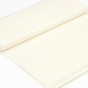 Puede incluir: Un rollo de tela de color crema, parcialmente desenrollado, que muestra una superficie lisa y opaca. La tela parece ser un material suave, adecuado para proyectos de costura o artesanía. El borde del rollo revela una etiqueta con texto.
