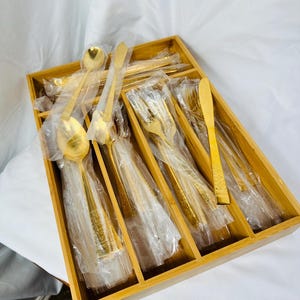 May include: A bamboo cutlery tray with gold-colored silverware, including forks, knives, and spoons, organized in individual compartments.