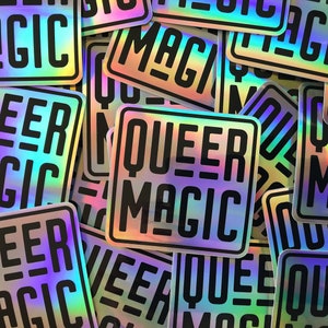 May include: A pile of iridescent holographic stickers with the text "Queer Magic" printed in black. The stickers are square shaped and have a rainbow sheen.