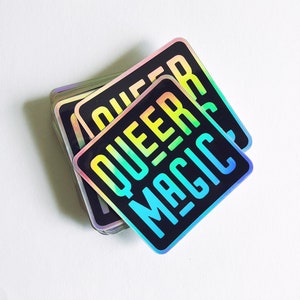 May include: A stack of rainbow holographic stickers with the text "QUEER MAGIC" in black.