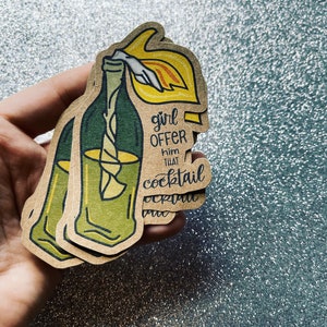 May include: A brown paper sticker with a green and yellow illustration of a bottle with a lit fuse. The text on the sticker reads "girl offer him that cocktail".
