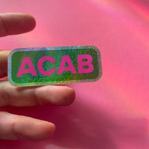 Puede incluir: Una pegatina holográfica verde y plateada con el texto "ACAB" en letras rosas.