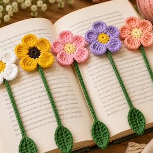 May include: Five handmade crochet flower bookmarks featuring long green stems with a single leaf at the base. The flowers have distinct centers and petals in white, yellow, pink, purple, and peach colors, resting on an open book page.