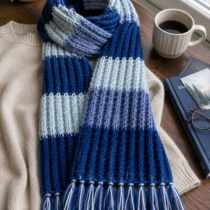 May include: A blue and white striped knitted scarf with fringe. The scarf is made of soft yarn and has a ribbed texture. The scarf is approximately 72 inches long.