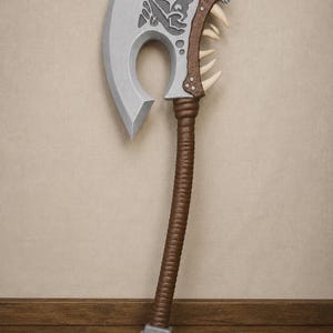 以下が含まれることがあります： グレーの刃と茶色の柄が付いたファンタジー風の斧。 斧の頭は、鋭い歯を持つ様式化された動物の頭のデザインが特徴です。 柄は質感があり、ベースは正方形の金属製の端が付いています。