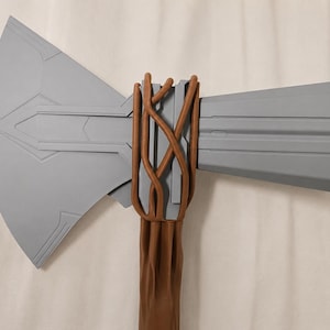 May include: A gray battle axe with a brown wooden handle. The axe head is a light gray color with geometric designs. The handle is wrapped with brown, vine-like material. The axe measures approximately 30 inches in length.