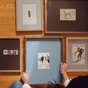 May include: A collection of five framed wall art pieces featuring a vertical striped print with three olives, a sketch of a dog, a triptych of wedding photos, a black and white wedding photo with a blue mount, and a Ralph Lauren ski poster.