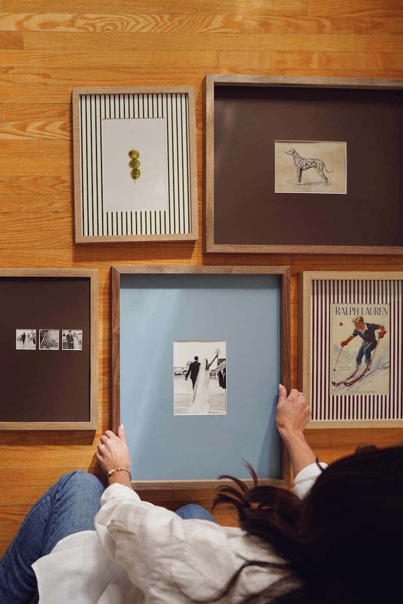 May include: A collection of five framed wall art pieces featuring a vertical striped print with three olives, a sketch of a dog, a triptych of wedding photos, a black and white wedding photo with a blue mat, and a Ralph Lauren ski poster.